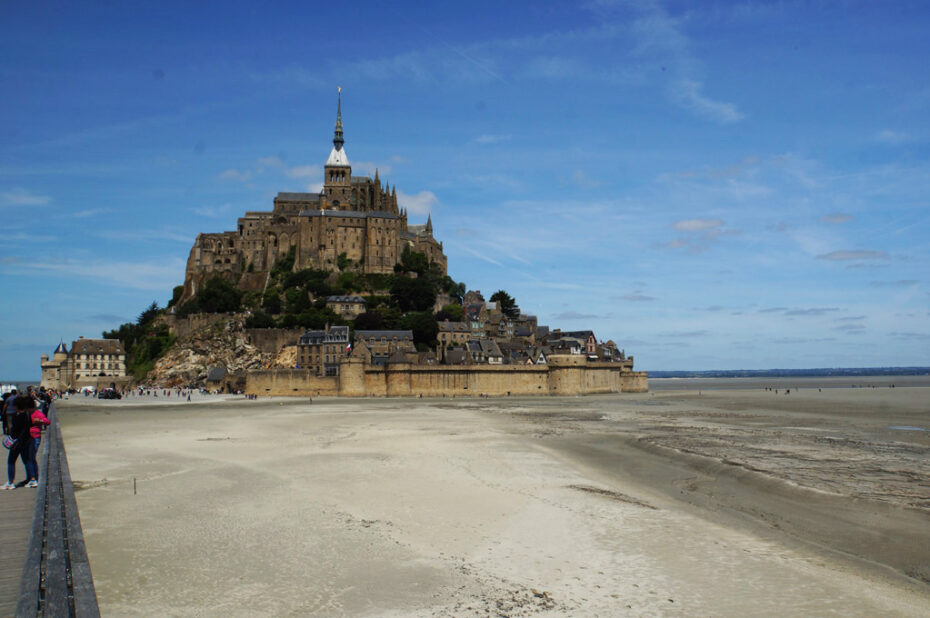 Photograph showing Mount Saint-Michel during ebb tide, surrounded by a vast mudplain.